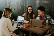 Three people talking in front of computers. A photo by Brooke Cagle on Unsplash.